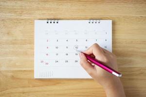 calendar page on table with female hand holding pen, top view photo