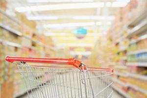 Supermarket aisle blurred background with empty red shopping cart photo