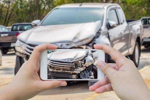 mujer que usa un teléfono inteligente móvil que toma una foto de un accidente automovilístico dañado para el seguro