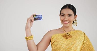 retrato de mulher tailandesa em traje tradicional, segurando o cartão de crédito. fêmea olhando para a câmera e sorrindo com fundo branco isolado. video