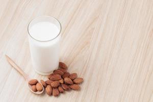 almond milk in glass on wood background with nuts around the bowl.selective focus.front view.copy space. photo