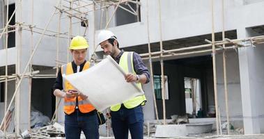 A Caucasian male and Asian man civil engineer holding a blueprint and working together video