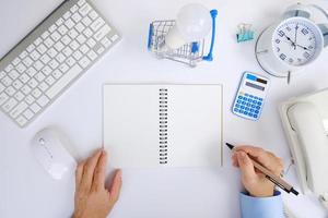 Office desk with smartphone, laptop computer, cup of coffee, and office tools. Flat lay, top view with copy space. A bank notepad and a pen are on top of an office desk table containing computer tools photo