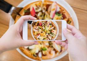 mujer tomando fotos de pizza con teléfono inteligente móvil