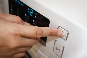 primer plano de la mano femenina tocando la pantalla digital, el panel de control de la lavadora automática, el botón de inicio o pausa. foto