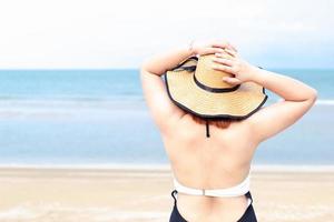 A woman standing with her back in a swimming dress and a sun hat on the beach.Beach vacation.Copy space. photo