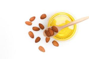 Yellow almond oil in a clear bowl with a wooden spoon next to it and several almonds on a white background.top view,top-down.flat lay. photo