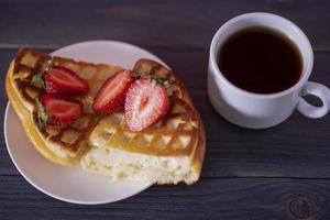 Belgian waffles with strawberries and coffee on a wooden, dark table. photo