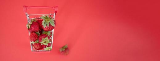 pequeño carro lleno de fresas maduras frescas sobre un fondo rojo. foto