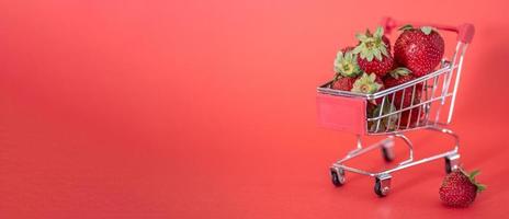 pequeño carro lleno de fresas maduras frescas sobre un fondo rojo.