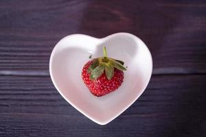 Strawberries in a heart-shaped plate on a wooden, dark background. photo