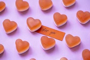 Red candy marmalade in shape of heart with a note FOR YOU on pink background. Sugar gummy candy. Valentine's Day concept. Geometric pattern. Minimal design, flat lay, top view. photo