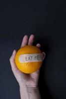 Female hand holding orange on black background. Citrus fruit with plaster note EAT ME. Healthy lifestyle concept. Vegetarian food and vitamins. photo