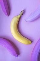 One yellow banana among colored pink bananas on pink background. Not such as all, unique concept. Closeup creative food pattern in minimal style. Flat lay, top view. photo