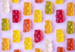 Colorful gummy bears on pink background. Orange, red and yellow jelly bears. Candy marmalade food. Geometric pattern. Minimal design, flat lay, top view. photo