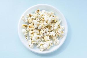 Tasty salted popcorn in plastic bowl on blue background. Cinema and entertainment concept. Close up, top view and shooting in studio. photo