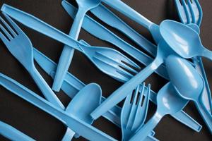 Plastic blue forks, spoons and knives on black background. Closeup concept plastic dishes, plastic pollution. Flat lay, top view. photo