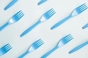 Many blue plastic forks on light background, top view. Disposable tablewear, sorting plastic concept. Creative pattern, flat lay photo