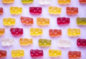 Sweet fruit gummy bears on pink background. Orange, red and yellow marmalade bears. Candy colorful pattern. Minimal design, flat lay, top view. photo