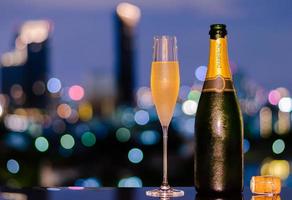 A glass with vapour of cold Champagne with bottle and cork on colorful city bokeh lights background. photo