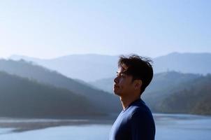 Asian man smiling and looking up with mountain any lake background. Good mental health concept. photo