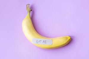 Yellow banana with plaster note EAT ME on pastel pink background. Minimal food concept. Flat lay, top view. photo