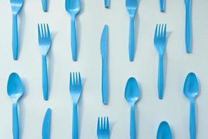 Many blue plastic forks, spoons and knives on light background, top view. Disposable tablewear, sorting plastic concept. Creative pattern, flat lay photo