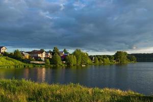 a village on the river bank with bright green grass and a beautiful sky. photo