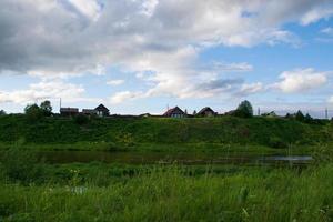 a village on the river bank with bright green grass and a beautiful sky. photo