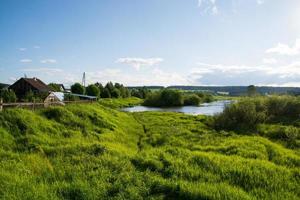 a village on the river bank with bright green grass and a beautiful sky. photo