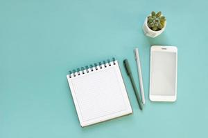 Top view of workspace and opened notebook with mock up blank pages on blue background. Flat lay photo