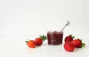 conservas de fresa caseras o mermelada en un tarro de albañil rodeado de fresas orgánicas frescas. enfoque selectivo con fondo blanco. foto