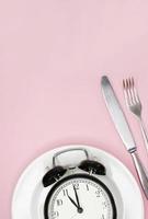 Concept of intermittent fasting, ketogenic diet, weight loss. fork and knife, alarmclock on plate photo
