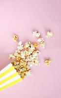 Spilled popcorn on pink background. Movie night concept. Copy space for text photo