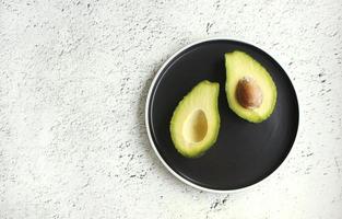 Avocado on black plate. Top view. Banner. Pop art design, creative summer food concept. Green avocadoes, minimal flat lay style. photo