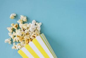 Spilled popcorn and paper bucket on blue background. Movie night concept. Copy space for text photo
