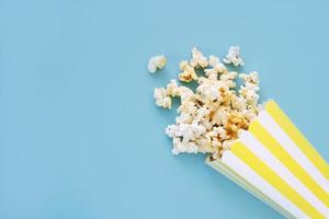 Spilled popcorn and paper bucket on blue background. Movie night concept. Copy space for text photo