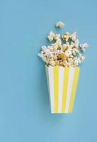 Spilled popcorn and paper bucket on blue background. Movie night concept. Copy space for text photo