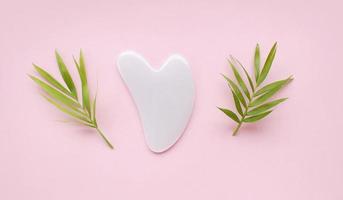 Top view of pink heart shaped guasha stone made of quartz crystal on pink background with copy space. Concept of alternative skin care treatment, self massage and acupressure photo