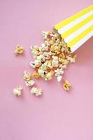 Spilled popcorn on pink background. Movie night concept. Copy space for text photo
