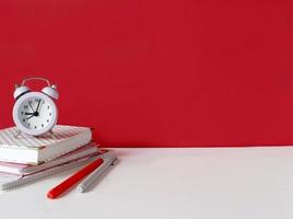 Creative desk with notebook, desk objects, office supplies, books, on white table, red wall. Student's desk. Creative workspace front view. Mock up photo