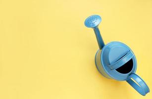 blue watering can on yellow background. Creative concept of investment, growth, success in business and life or hello summer. Top view Flat lay photo