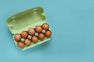 Organic eggs in cartons tray on blue background. Flat lay, top view photo