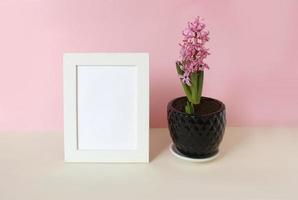 photo frame with white blank card and flowers on pastel pink background. Mock up poster frame. Stylish template.