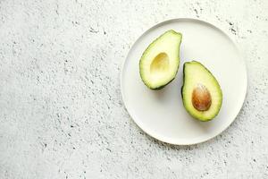 Avocado on white plate. Top view. Banner. Pop art design, creative summer food concept. Green avocadoes, minimal flat lay style.