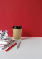 Creative desk with notebook, desk objects, office supplies, books, on white table, red wall. Student's desk. Creative workspace front view. Mock up photo