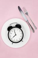 Concept of intermittent fasting, ketogenic diet, weight loss. fork and knife, alarmclock on plate photo