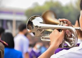 estudiante asiático joven que sopla una trompeta con la banda de música de la escuela, fondo borroso foto