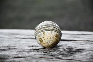 antiguos equipos deportivos de cricket de entrenamiento en suelo oscuro, pelota de cuero, wickets, casco y bate de madera, enfoque suave y selectivo, concepto tradicional de amantes del deporte de cricket en todo el mundo. foto