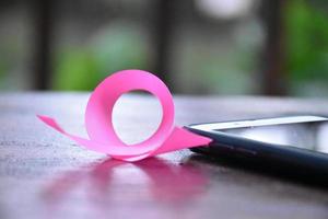 Pink ribbon on table with mobile phone. Concept for protesting and supporting the breast cancer against in woman. photo